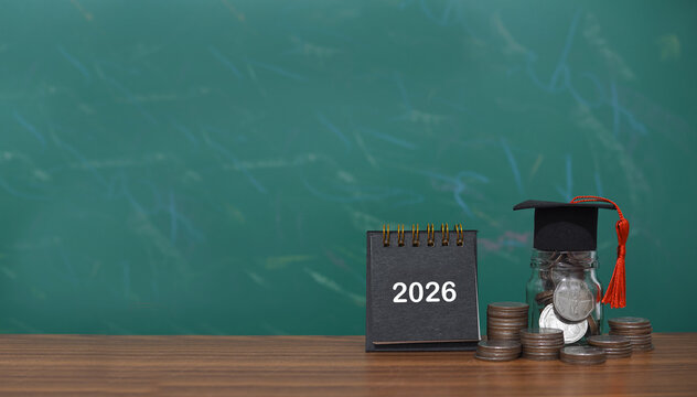 Study goals, 2026 Desk calendar, Glass bottle with graduation hat and stack of coins. The concept of saving money for education, student loan, scholarship, tuition fees in New Year 2026