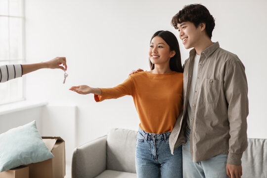 Cheerful millennial couple smiles as they receive their new house keys from the seller on a bright moving day. They are excited and ready to start their new chapter in life.