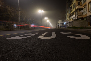 Bold letters spell out BUS on the ground in a city. Night scene.