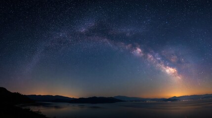 Fototapeta premium Bright stars and the Milky Way stretch across the night sky above a calm lake. Distant mountains create a serene backdrop, enhancing the beauty of the scene during nighttime.