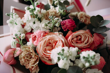 Soft natural light bouquet of pastel roses, carnations and white flowers with eucalyptus in elegant wrapping, close-up romantic still life without people