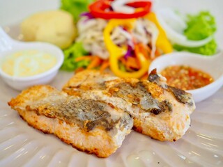 Salmon steak and vegetable salad with salad dressing and seafood sauce placed on a plate. Healthy food.