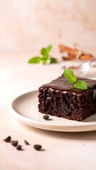 Chocolate brownie on a plate, glazed with ganache, garnished with mint leaves