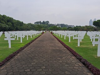 
Ereveld Ancol war cemetery in Jakarta, Indonesia, with neatly arranged white gravestones surrounded by green lawns and trees, creating a solemn and peaceful memorial atmosphere.