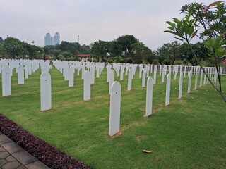 Ereveld Ancol war cemetery in Jakarta, Indonesia, with neatly arranged white gravestones surrounded by green lawns and trees, creating a solemn and peaceful memorial atmosphere.