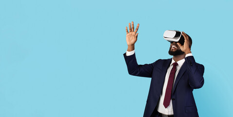 Virtual Reality Experience. Amazed Black Businessman Playing Video Game In VR Glasses, Excited African American Male In Suit Standing Over Blue Studio Background, Panorama With Copy Space
