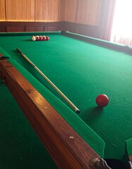 A close-up of a pool table showcasing green felt, wooden trim, a cue stick, and a single red ball with other balls lined up