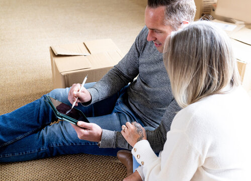 Man sitting on the carpeted floor holding a tablet and stylus with wife beside him