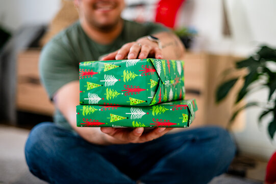 A man in his thirties presents two wrapped Christmas gifts