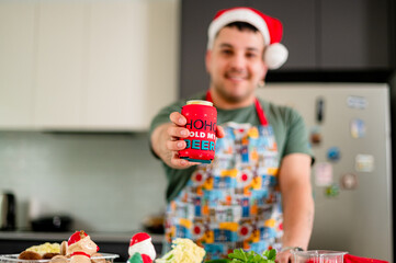A man in a vibrant apron prepares a colourful Christmas meal, showcasing beer in stubby holder