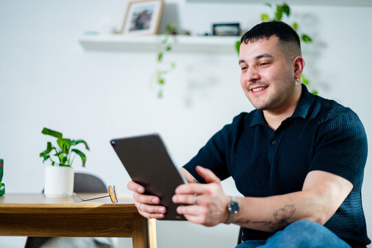 Adult man engages with a tablet in a stylish living space, smiling as he explores content
