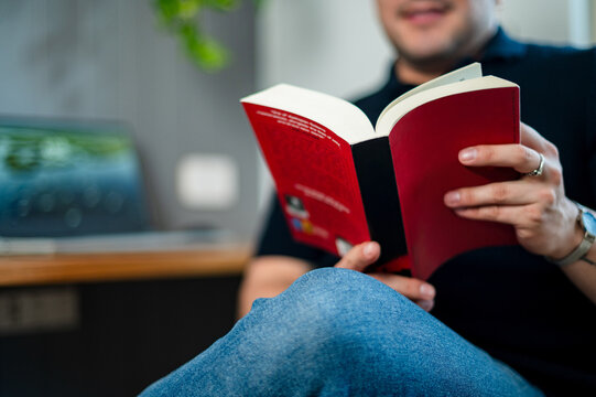 A man in his thirties relaxes while reading a book in a home office environment