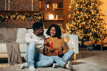 Young black couple sits on the floor, enjoying coffee together during the Christmas festivities....
