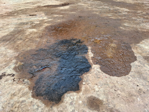 Dark black oil or chemical stain spilled on a rough concrete floor, indicating pollution, hazard, and industrial waste. Liquid spill and messy texture background