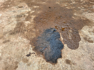 Dark black oil or chemical stain spilled on a rough concrete floor, indicating pollution, hazard, and industrial waste. Liquid spill and messy texture background
