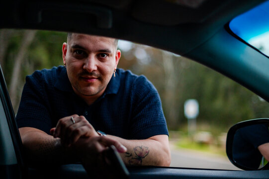 A man leans on a car window form outside vehicle in a park setting