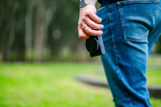 A man in his 30s holds a camera, capturing moments in a sunny park setting