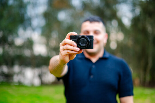 A man in his thirties smiles while taking a picture in a park during daylight