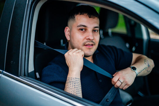 A man in his 30's sits in a car, fastening his seatbelt while parked at a park