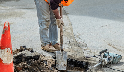 A plumber working on the street road opening asphalt using special equipment.