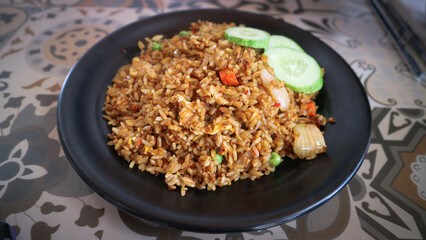 Fried rice on a black plate served with cucumber slices