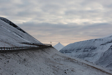 Longyerbeyen, Svalbard, Snowy mountain with a road that goes down the side of it. The road is empty and the sky is cloudy