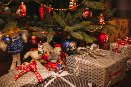 Cozy Christmas scene with decorated tree, colorful ornaments, plush toys and wrapped gifts with ribbons arranged underneath in warm indoor light