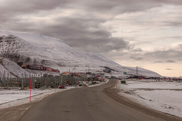 Longyerbeyen, Svalbard, Snowy road with a few cars on it. The road is surrounded by mountains and a small town