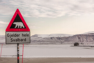 Longyerbeyen, Svalbard, Sign with a polar bear on it warns drivers to be careful. The sign is in a snowy area with mountains in the background