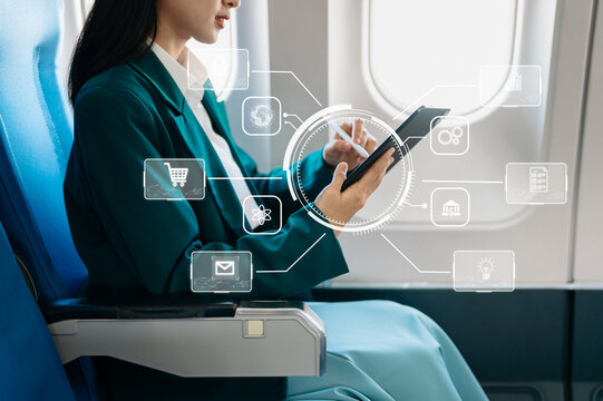 Asian businesswoman using tablet with digital interface icons during airplane flight. Concept of technology, innovation, and smart business travel.