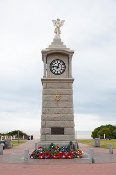 War memorial clock tower adorned with wreaths commemorating ANZAC Day and remembrance, standing under an overcast sky