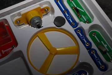 ​A close-up of the components of an educational electronic construction kit in a plastic tray, including a yellow electric motor, a propeller, and multicolored modules with snap connectors.