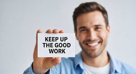 A smiling young man with a friendly expression holding a sign that says 'Keep Up the Good Work' in a bright, modern setting to motivate and inspire positivity