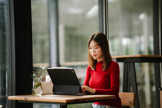 A woman wearing headphones works on a tablet in a cozy café, focused and relaxed by the window.
