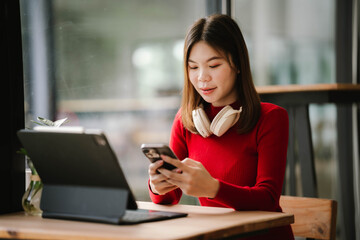 A woman wearing headphones works on a tablet in a cozy café, focused and relaxed by the window.