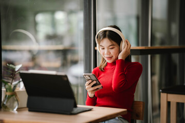 Fototapeta premium A woman wearing headphones works on a tablet in a cozy café, focused and relaxed by the window.