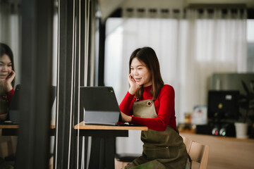 A smiling barista in a red sweater and apron holds a tablet while standing inside a cozy coffee shop.