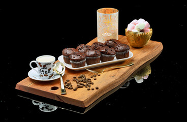 Delicious muffins and Marshmallows with coffee on a wooden board, on a black reflective surface
