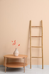 Wooden ladder, table and vase with lagurus near beige wall in room