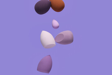 Flying different makeup sponges on purple background
