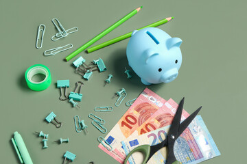 Different school stationery, piggy bank and money on green background
