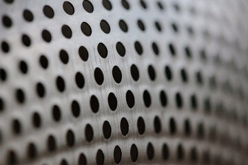 Close-up on a metallic perforated surface or metal grate with uniformly sized black circular holes,...
