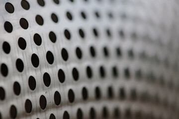 Close-up on a metallic perforated surface or metal grate with uniformly sized black circular holes,...