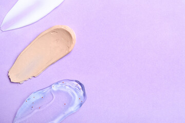 Samples of cosmetic cream, scrub and makeup foundation on lilac background