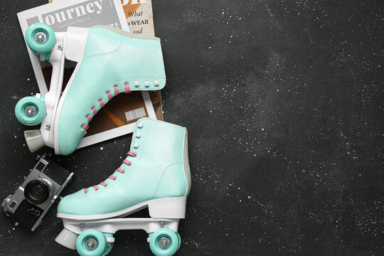 Composition with pair of vintage roller skates, magazines and photo camera on dark background