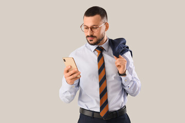 Young businessman with tie using mobile phone on light background