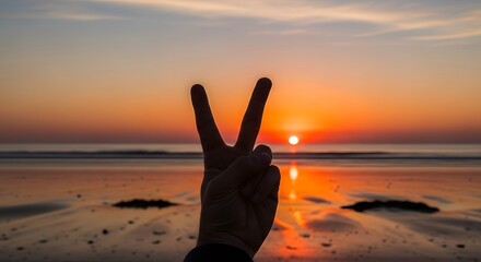 Hand Making Peace Sign at Sunset Over Ocean Beach with Vibrant Colors