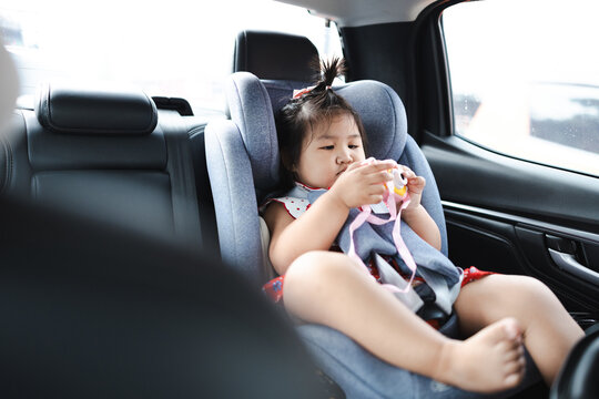 Cute little Asian girl sitting in a child car seat is having fun playing with a toy camera during a travel trip.