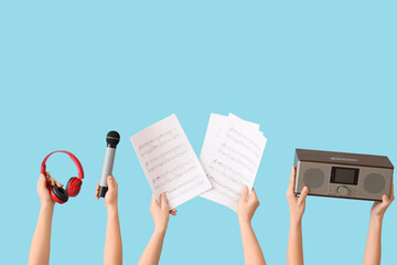 Female hands holding music sheets with microphone, radio receiver and headphones on blue background