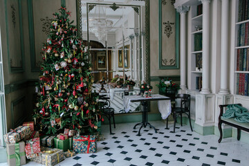 Elegant living room interior decorated for Christmas with a large decorated tree, a pile of presents, and a tiled black and white floor